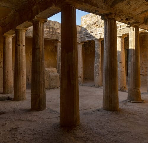 Ancient stone courtyard with tall columns and weathered walls, illuminated by sunlight from an open roof