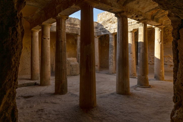Ancient stone courtyard with tall columns and weathered walls, illuminated by sunlight from an open roof