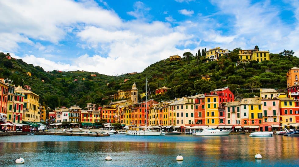 Panorama of Portofino town with pastel coloured houses, blue sea, white boats and green cliffs.