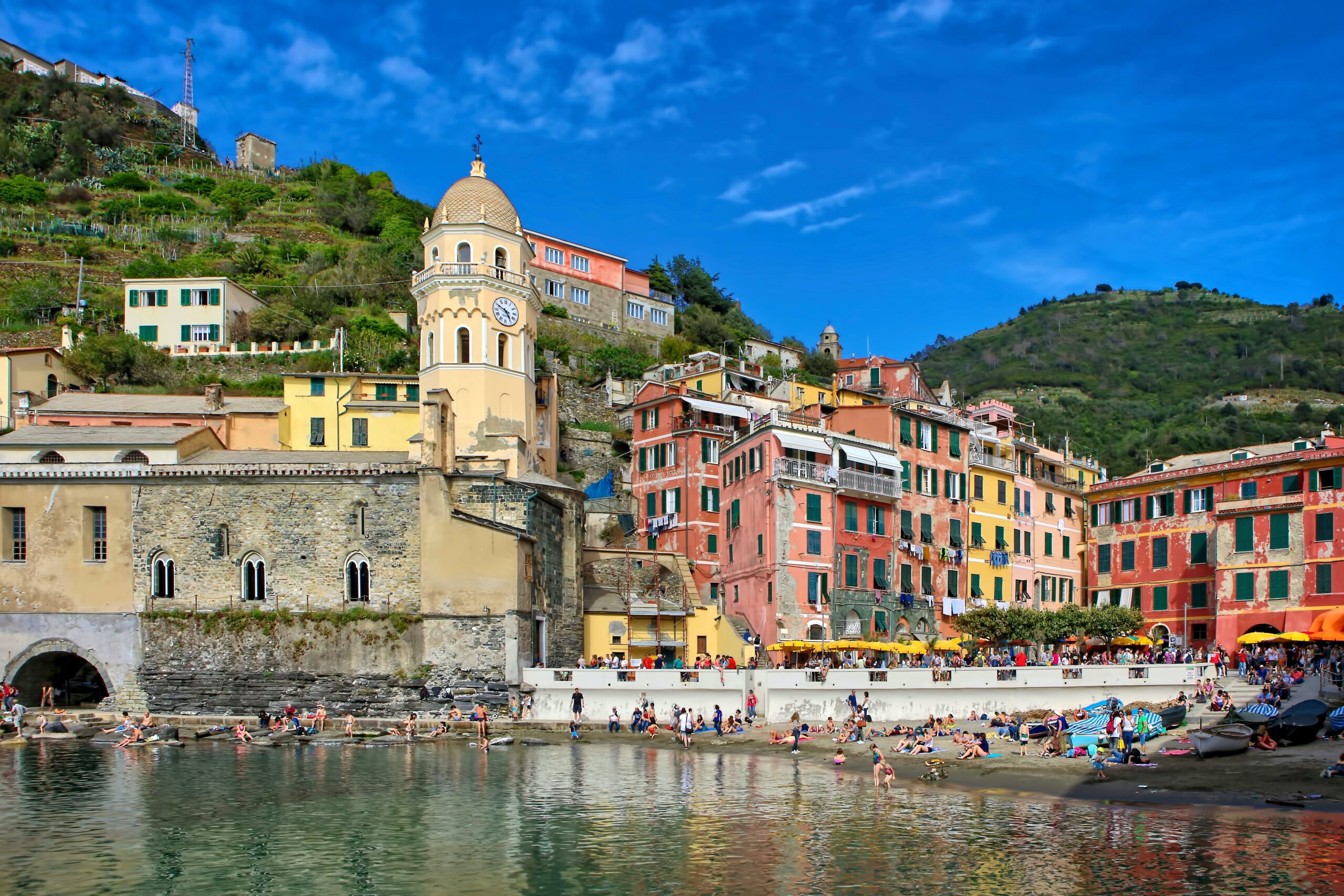 Colourful Italian town with people on the beach and a clock tower. This is Vernazza, one of the 5 towns of cinque terre.