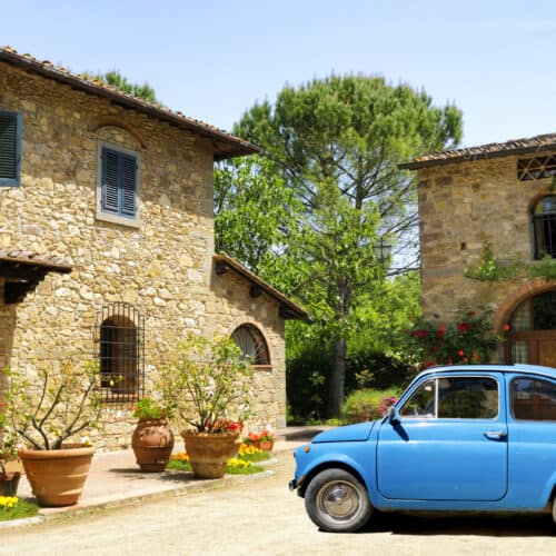 a blue rental car parked in front of a stone building in Italy.