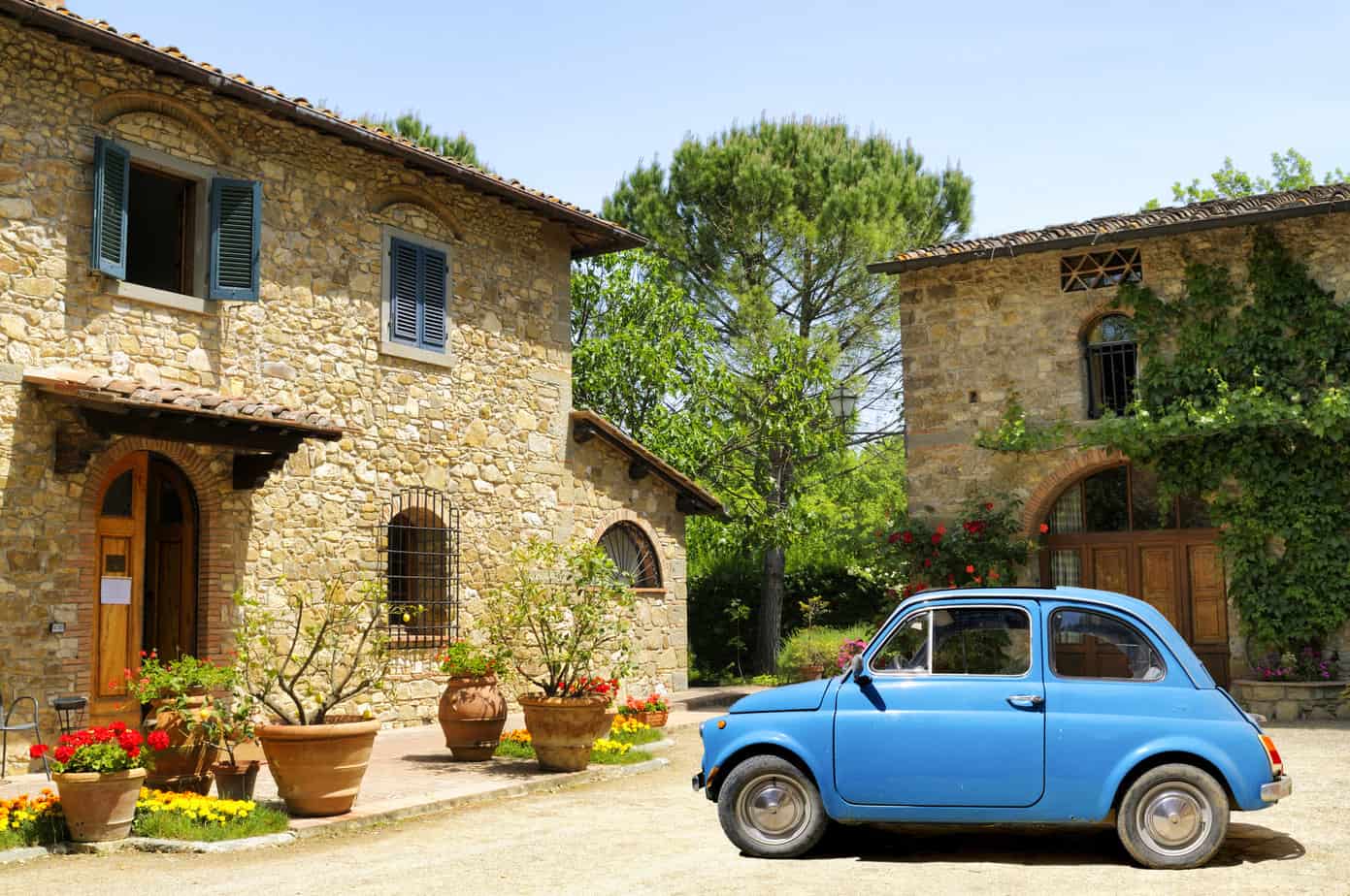 a blue rental car parked in front of a stone building in Italy.