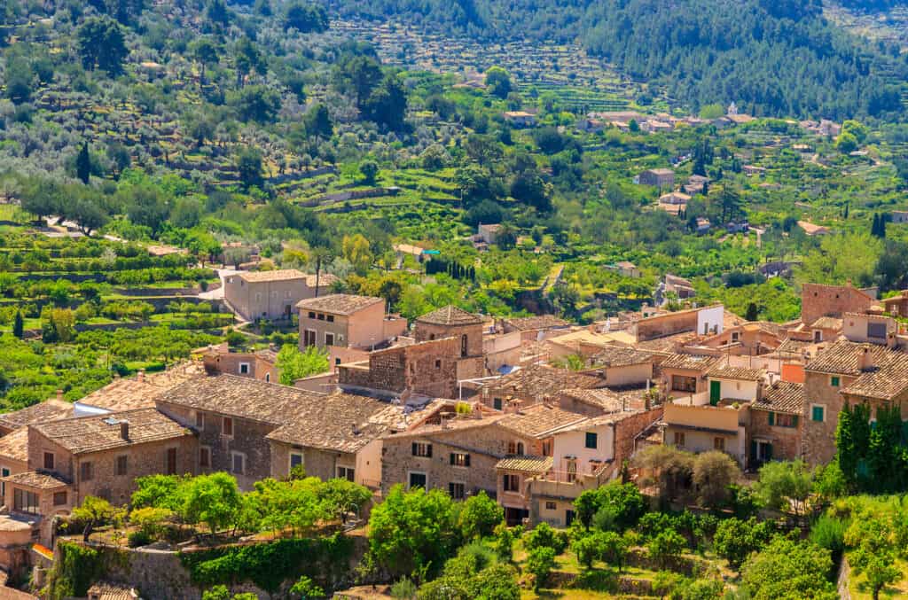 Aerial view of the picturesque village of Fornalutx, where rustic stone buildings nestle amid lush green terraced fields in a breathtaking mountainous landscape.