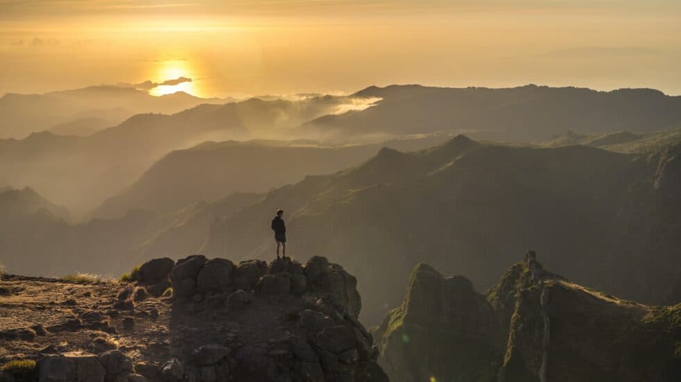 A man standing on top of a mountain at sunset.