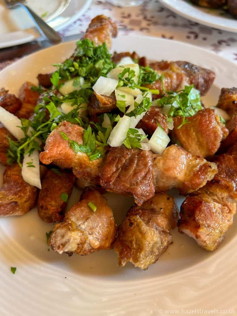 A plate of grilled meat pieces garnished with chopped onions and fresh herbs, served on a white dish, in Cyprus on a Troodos day trip.