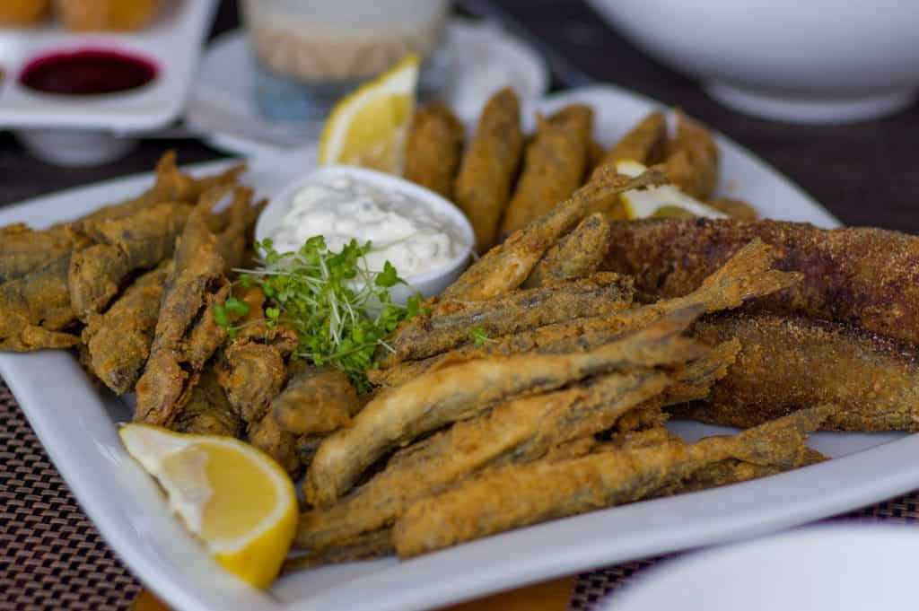 A plate of assorted fried fish with lemon wedges, a small bowl of tartar sauce, and a garnish of microgreens.