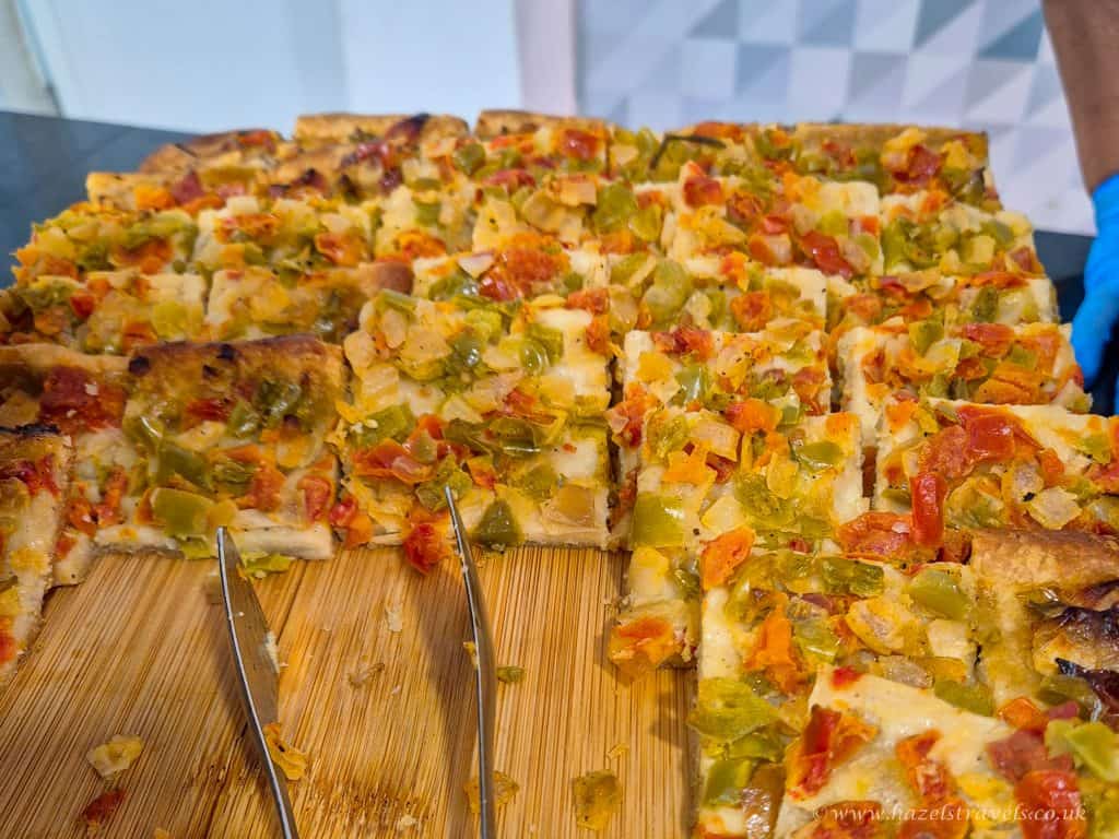 Savoury vegetable pizza slices topped with diced peppers, tomatoes, and cheese on a wooden cutting board, ready to serve at a casual dining event.