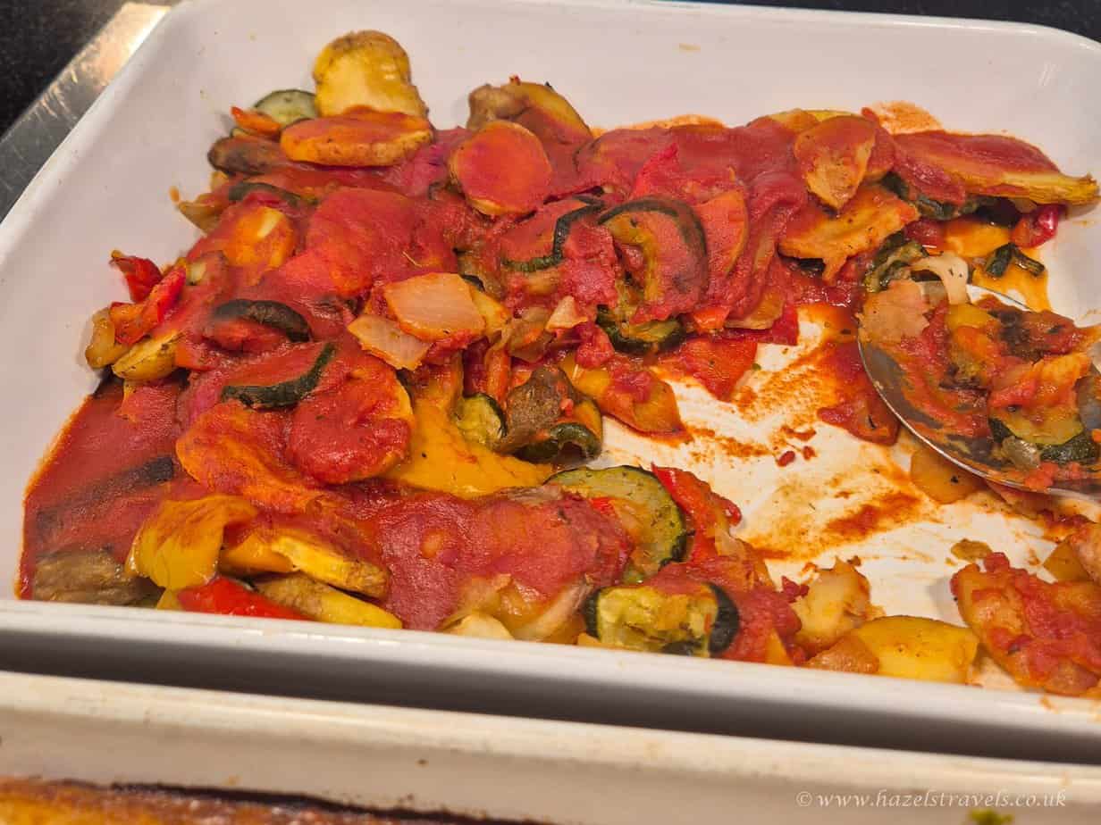 Roasted vegetable ratatouille dish with tomatoes, courgettes, aubergines, and peppers, served in a white baking dish. Perfect for plant-based travel cuisine and healthy eating.