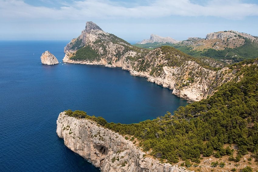 Mountain range in Mallorca from above, with a deep blue sea and light blue sky with white wispy clouds.