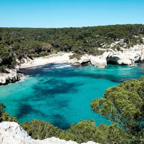 Beautiful turquoise coastal bay with white cliffs and lush green trees under a clear blue sky.