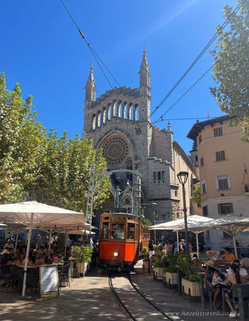 Colorful street scene in Geneva with a vintage tram, outdoor café, and the iconic St. Pierre Cathedral under a clear blue sky, showcasing Swiss city life and transportation.